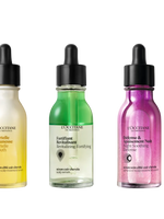 Three L'Occitane hair serum bottles in yellow, green, and pink on a white background